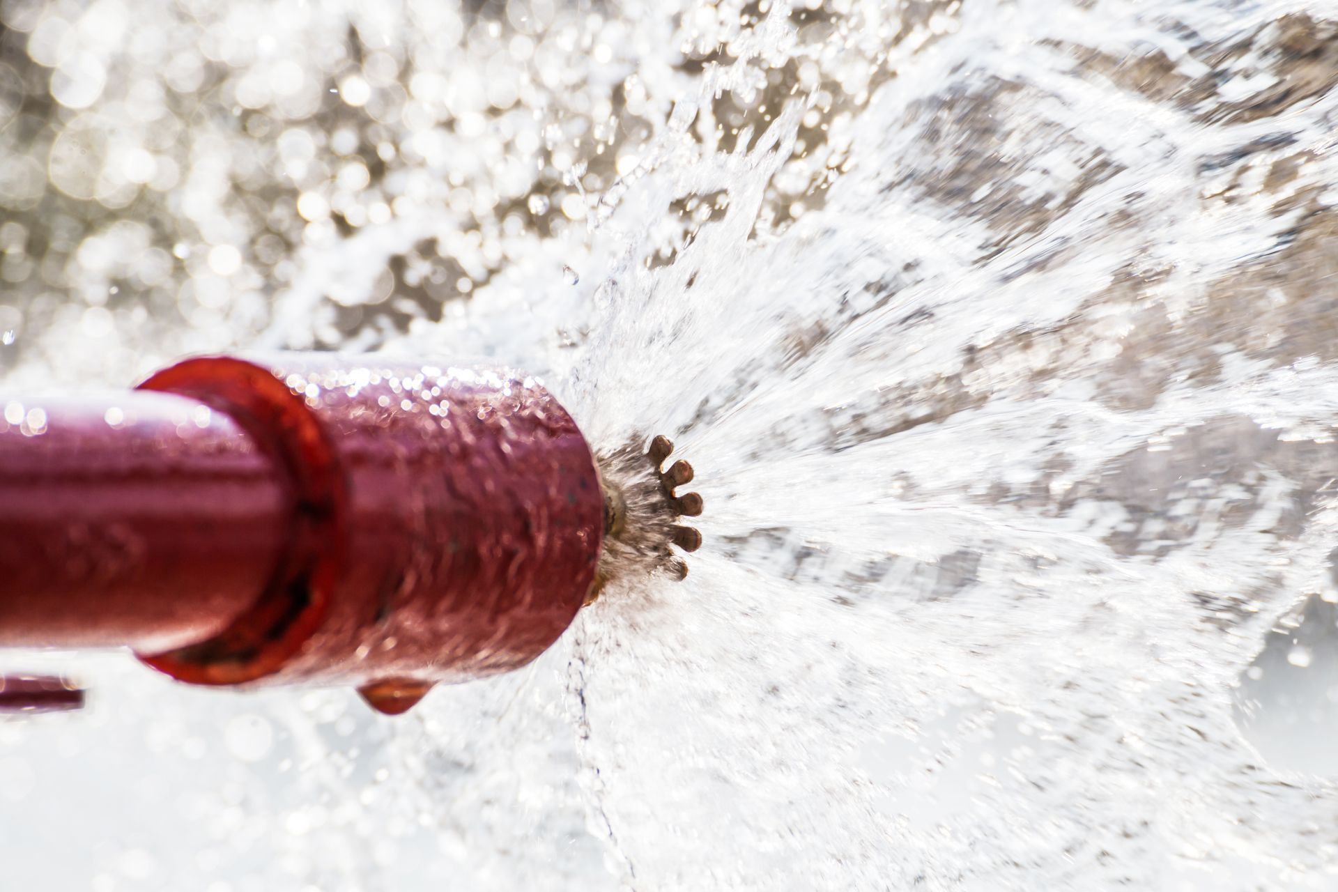 A fire sprinkler is spraying water from a red pipe.