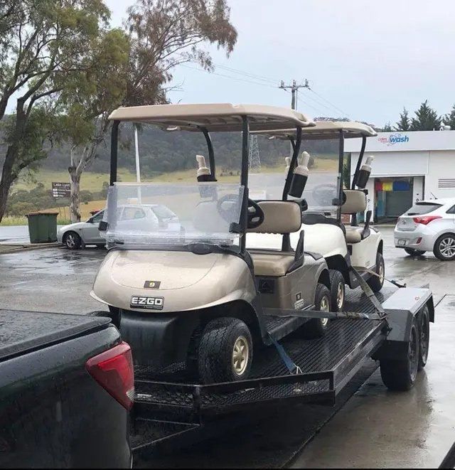 Two Beige Golf Carts on a Black Trailer, Ready for Transport — Orange Auto Electrics in Orange, NSW