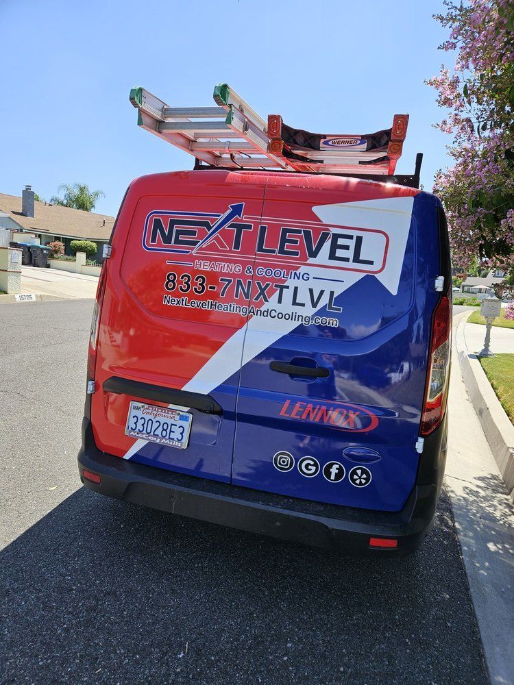 Red, white, and blue Next Level Roofing van with a ladder on top parked on a street.