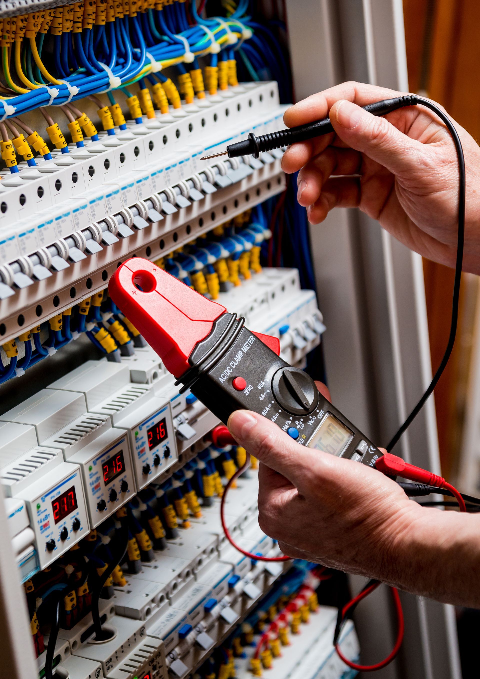 Electrician using a multimeter on electrical wiring in a panel, checking voltage. Electrician using a multimeter on electrical wiring in a panel, checking voltage.