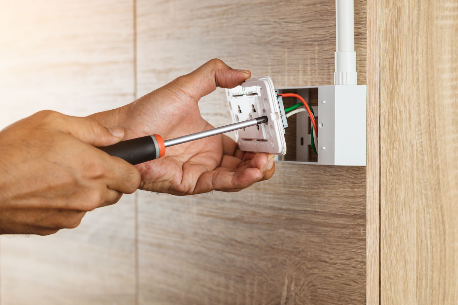 Person installing electrical outlet with screwdriver on wooden wall.
