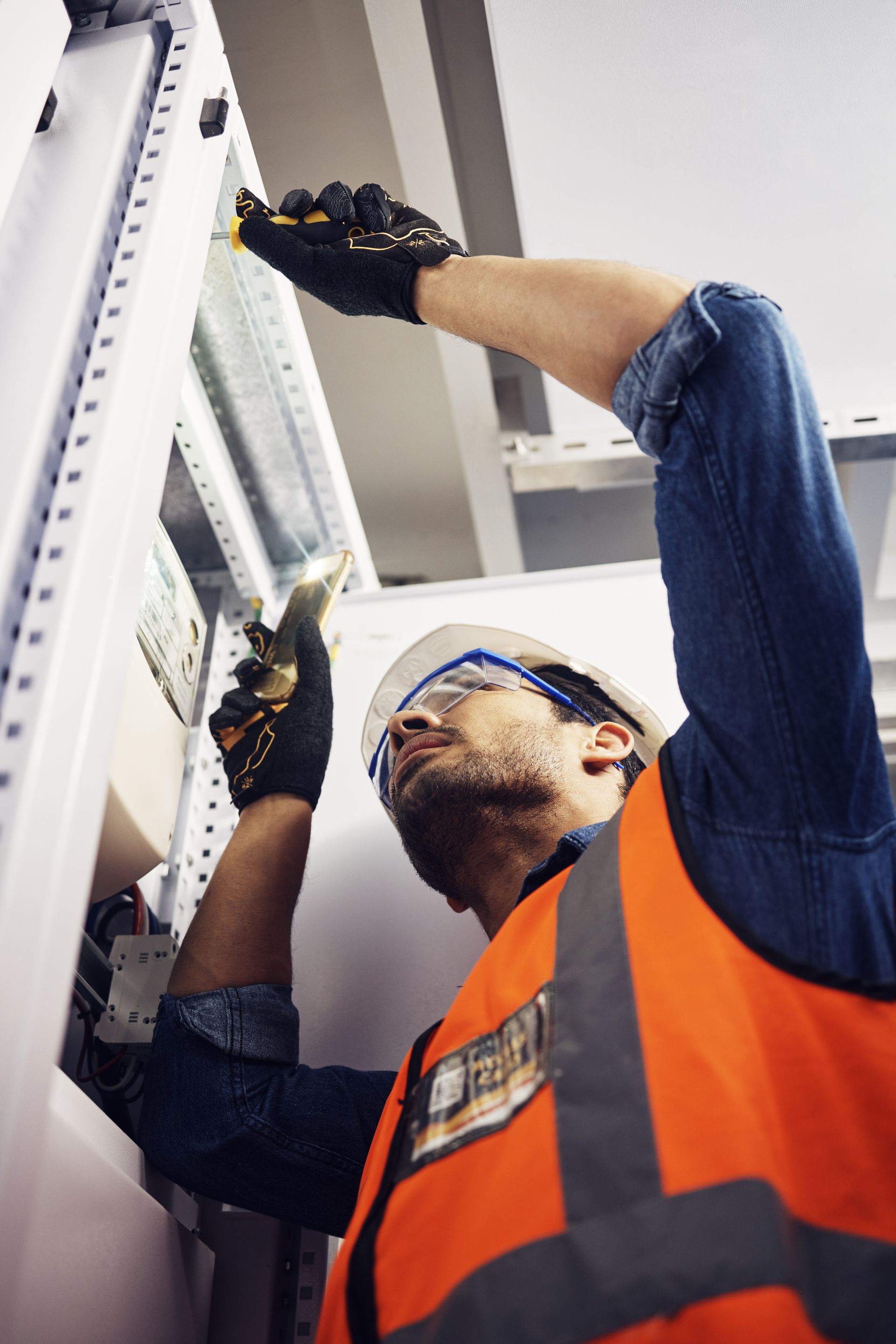 Electrician in safety vest and gloves working on a panel. Electrician in safety vest and gloves working on a panel.