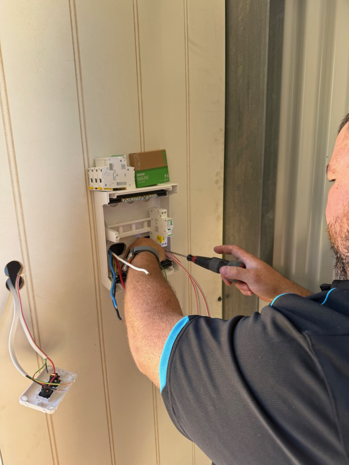 Electrician working on wiring inside a white box, using pliers and a screwdriver; blueprints in background. Electrician working on wiring inside a white box, using pliers and a screwdriver; blueprints in background.
