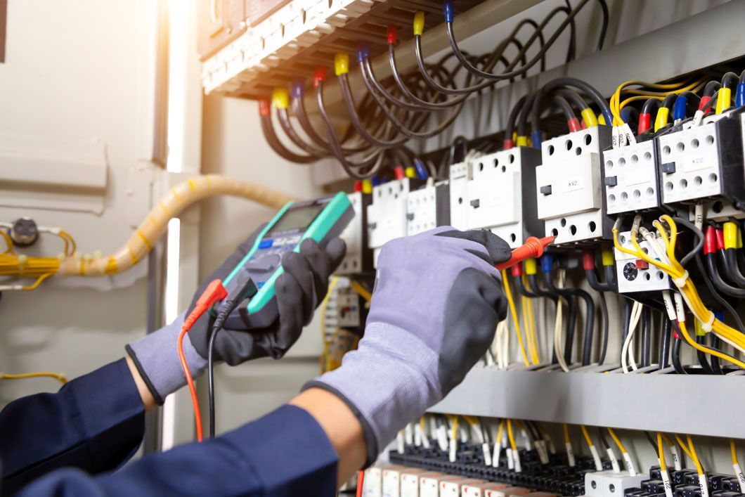 An electrician is working on an electrical panel with a multimeter.