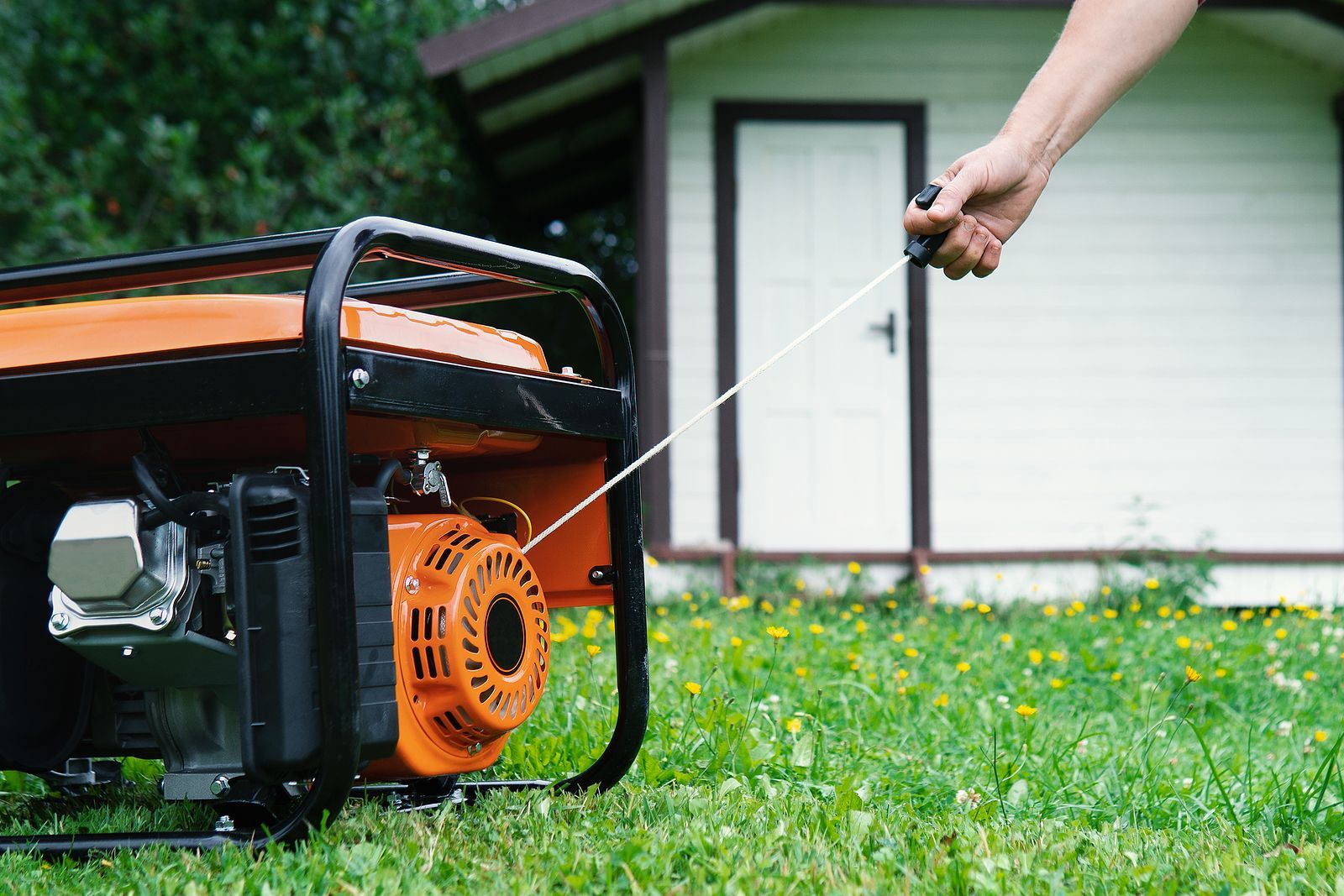 A person is pulling a rope to start a generator in front of a house.