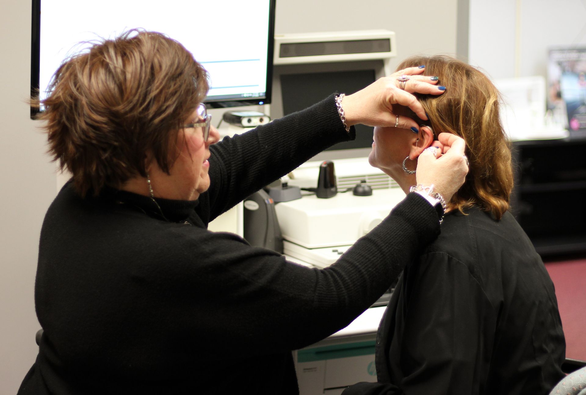 A woman is putting a hearing aid in another woman's ear.