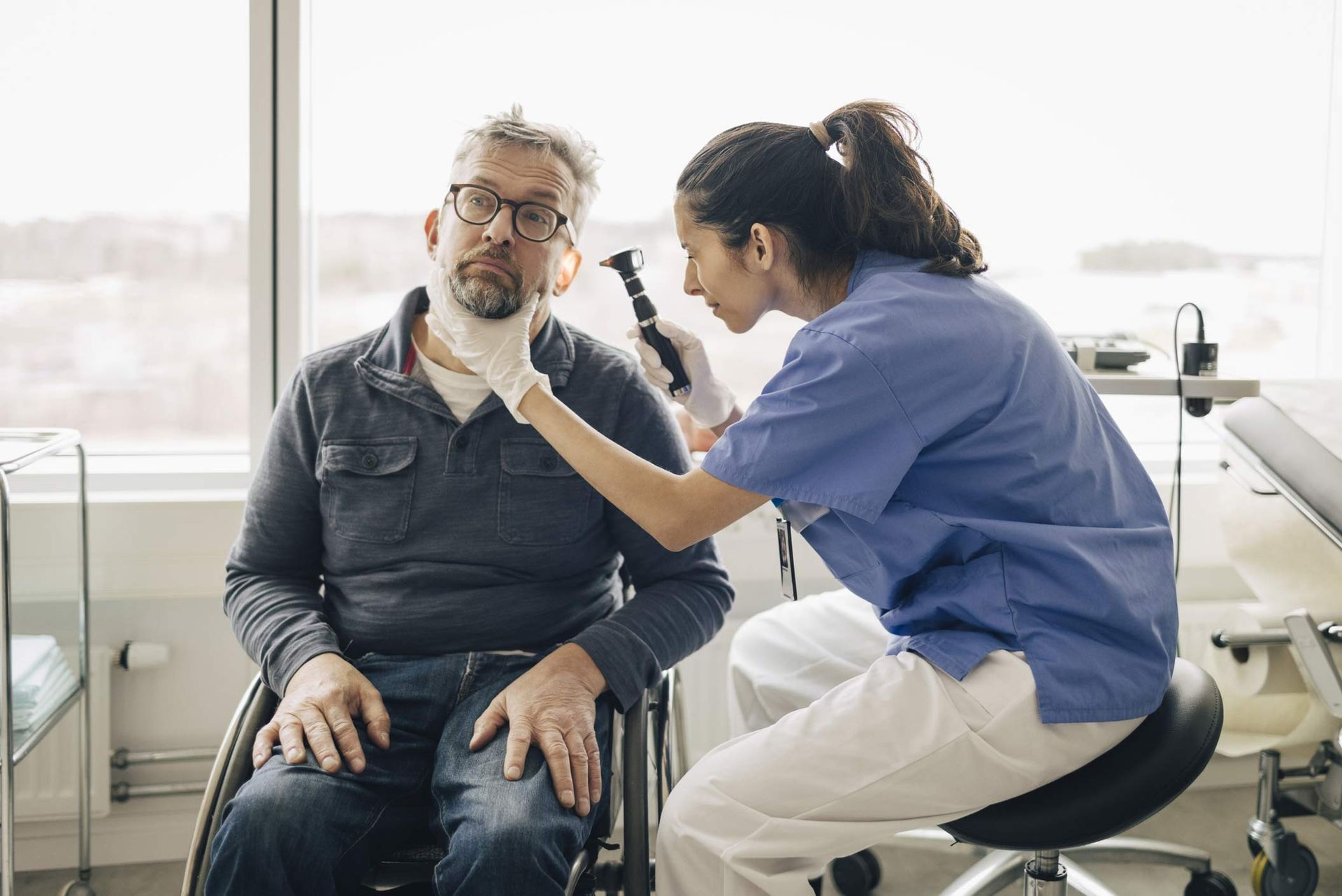 Side view of female Otolaryngologist examining ear of male patient with disability in medical room.