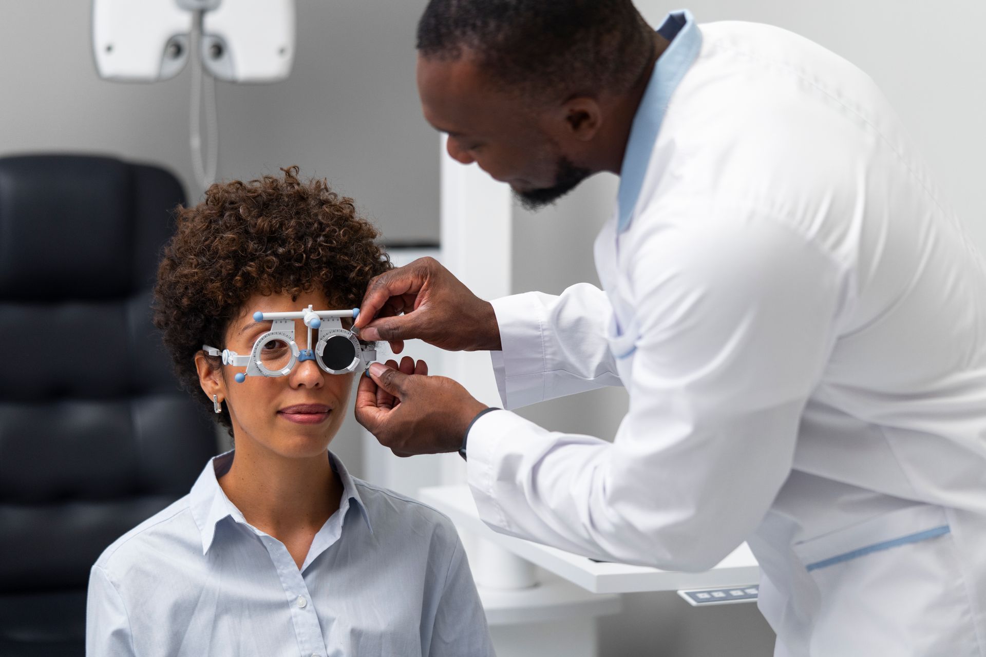 An optometrist adjusting a trial frame on a woman during an eye exam in a clinic.