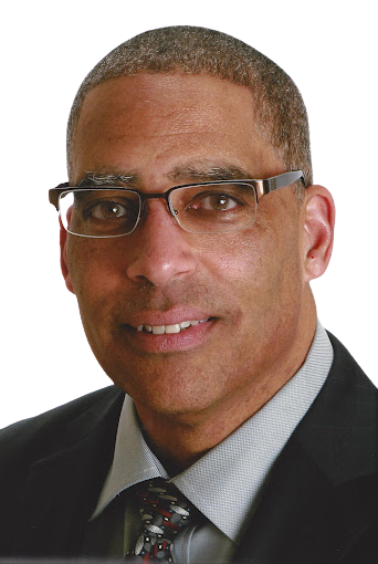 Man with glasses wearing a suit smiles at the camera.