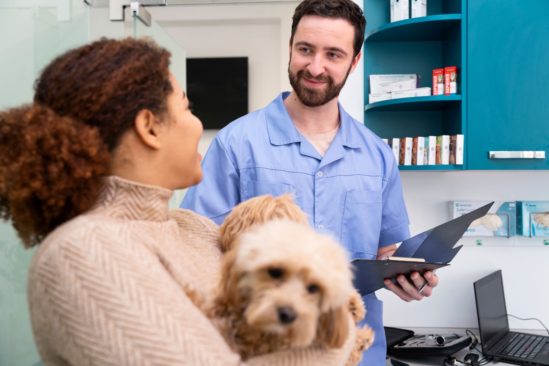 Woman holding dog, talking to vet in blue scrubs, in a clinic.