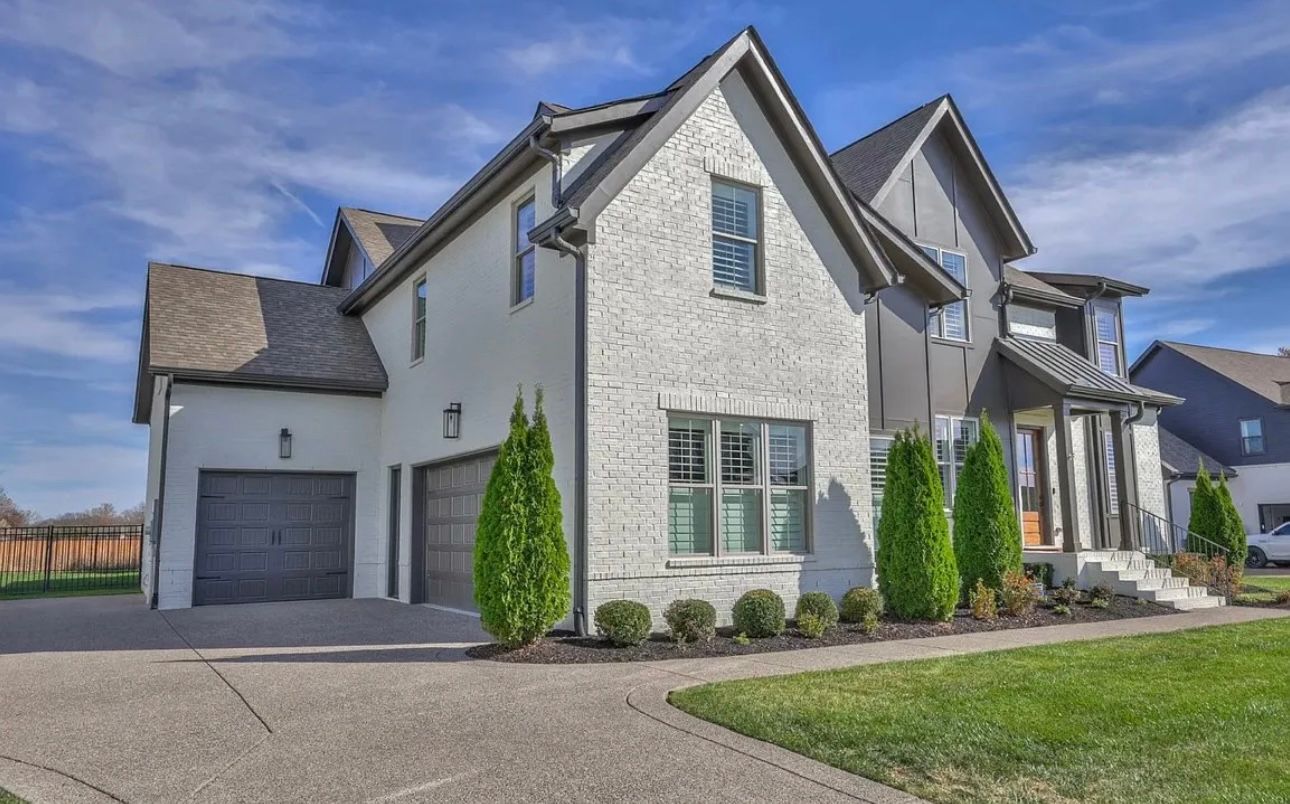 A large white brick house with a black garage door is sitting on top of a lush green lawn.