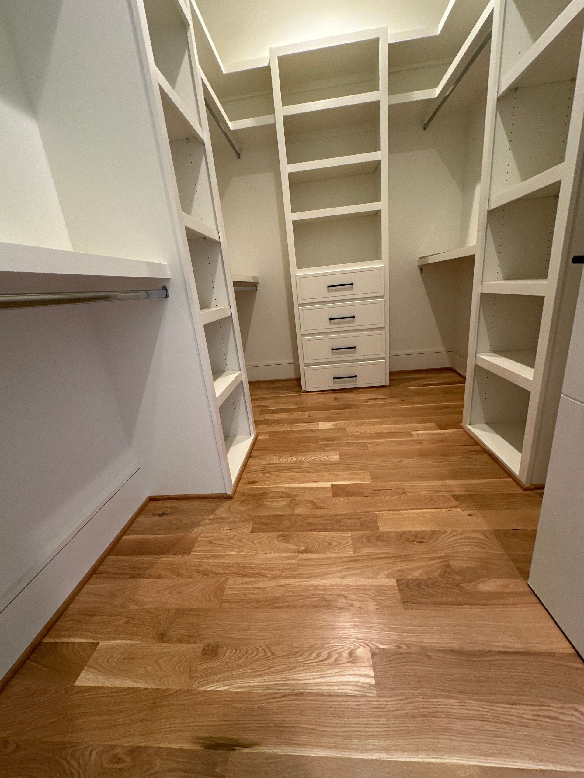 A walk in closet with hardwood floors and white shelves.