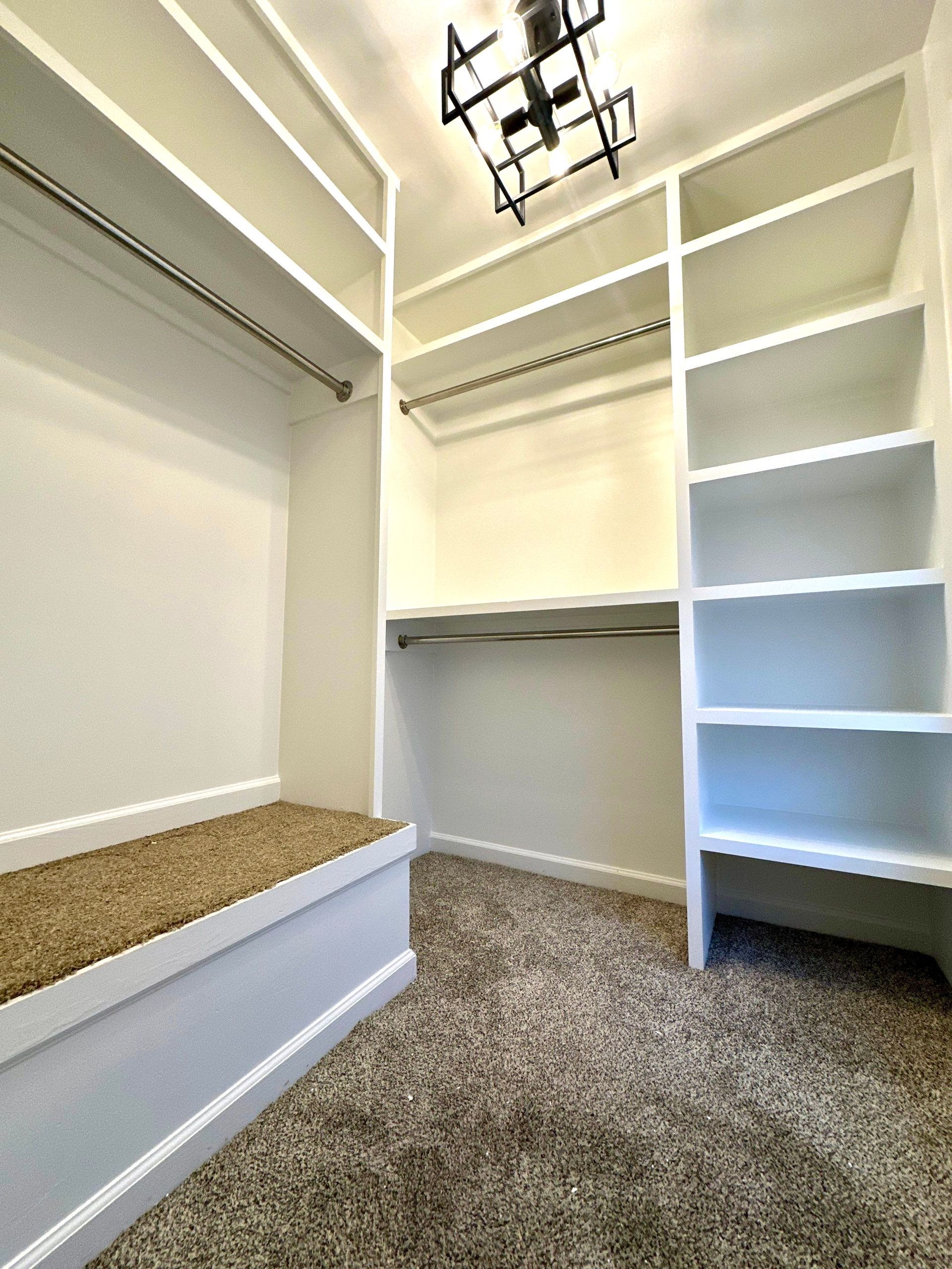 A walk in closet with lots of shelves and a bench