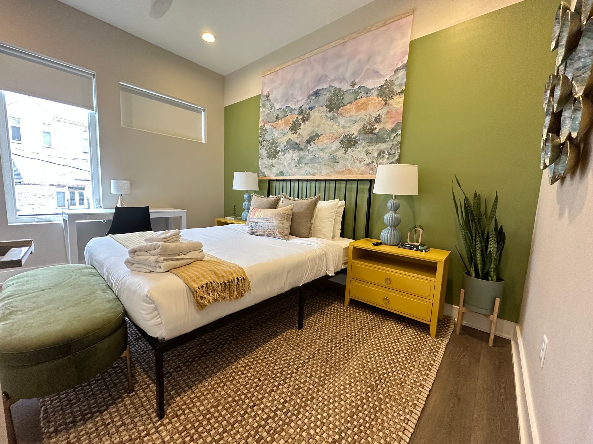 A bedroom with a bed , nightstand , ottoman and a large painting on the wall in Nashville, TN