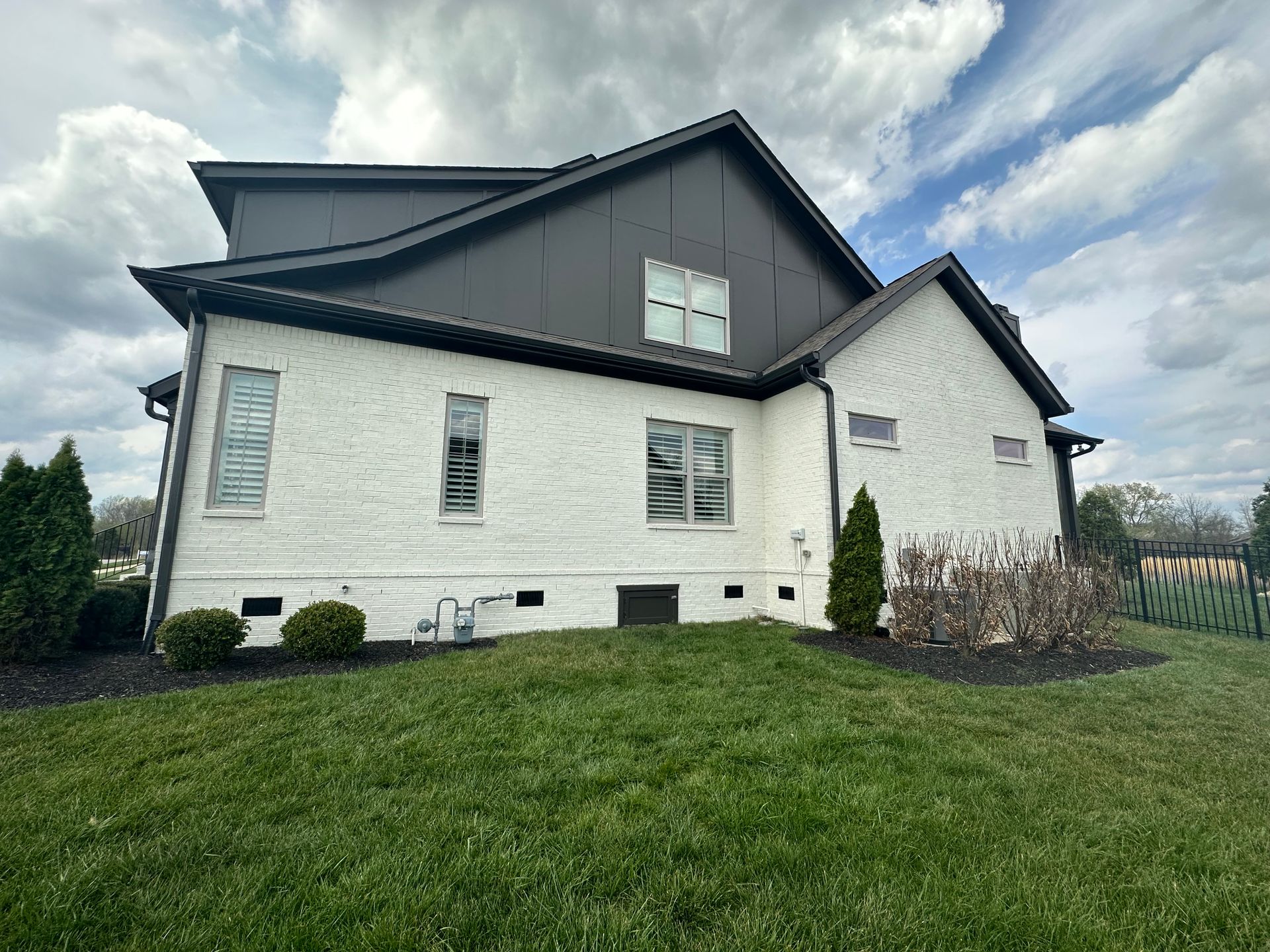 Exterior House Painting Services A large white house with a black roof is sitting on top of a lush green field.