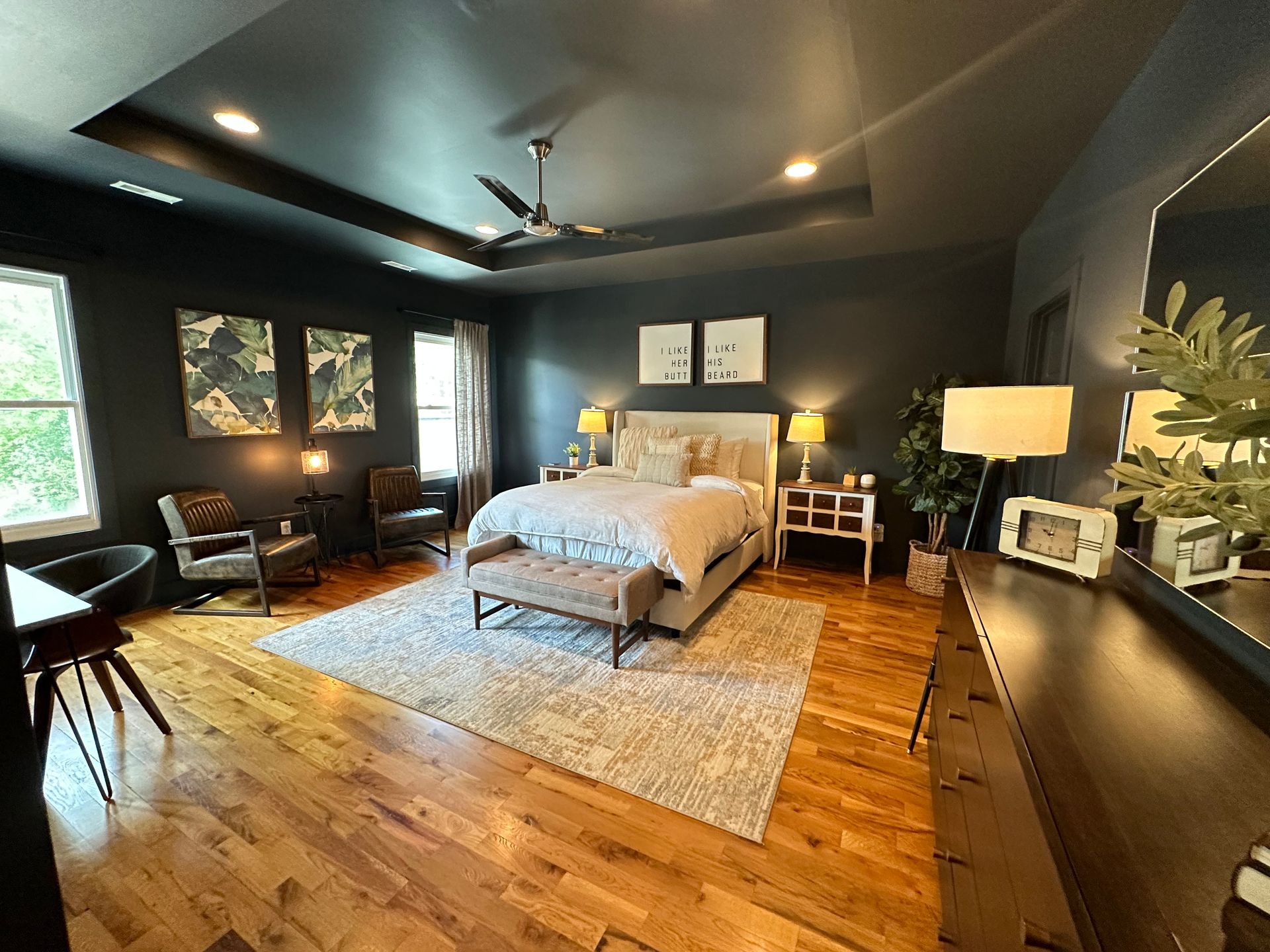 A bedroom with a large bed , dresser , chairs , and a ceiling fan.