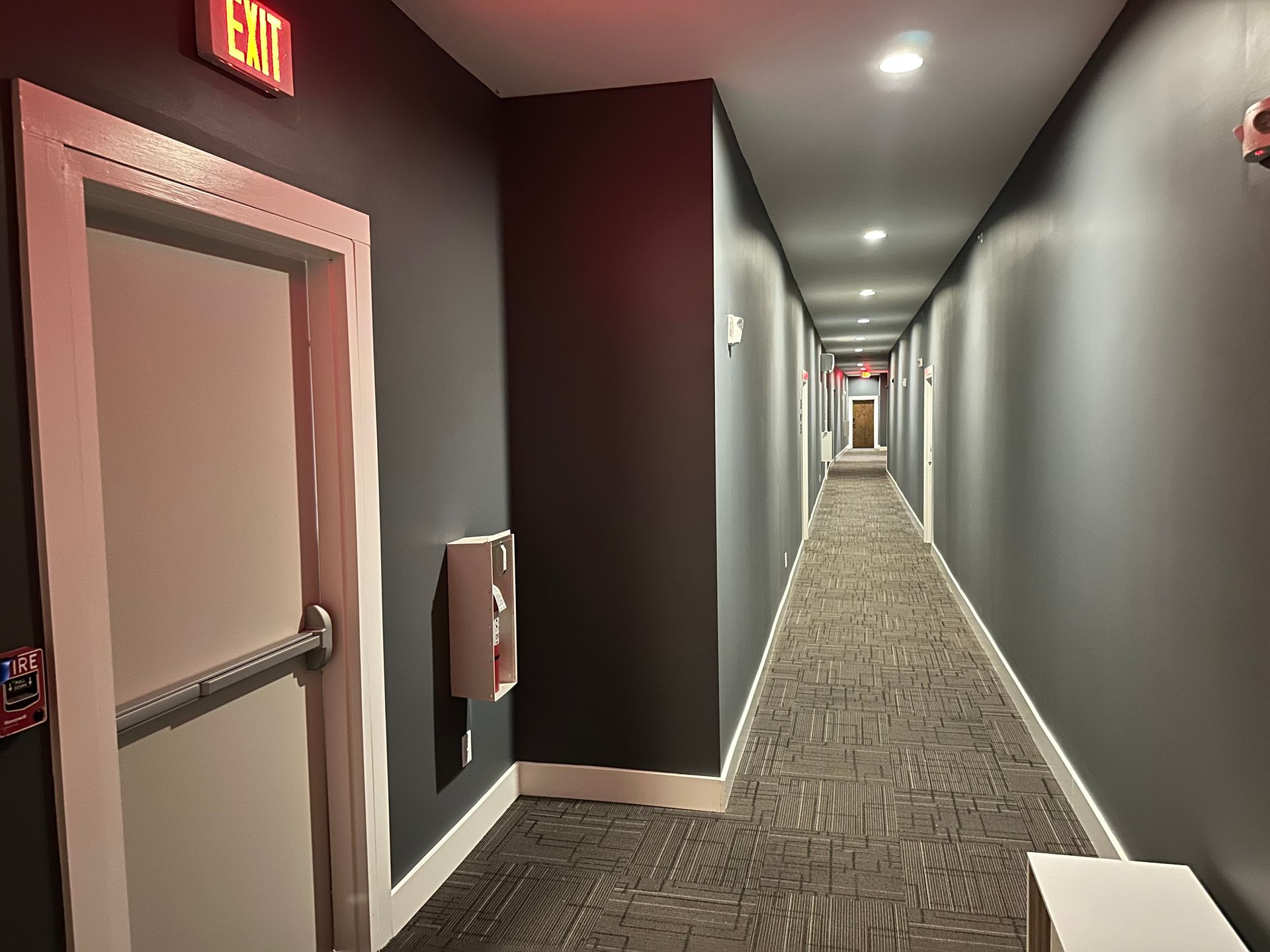 A long hallway with a red exit sign on the wall