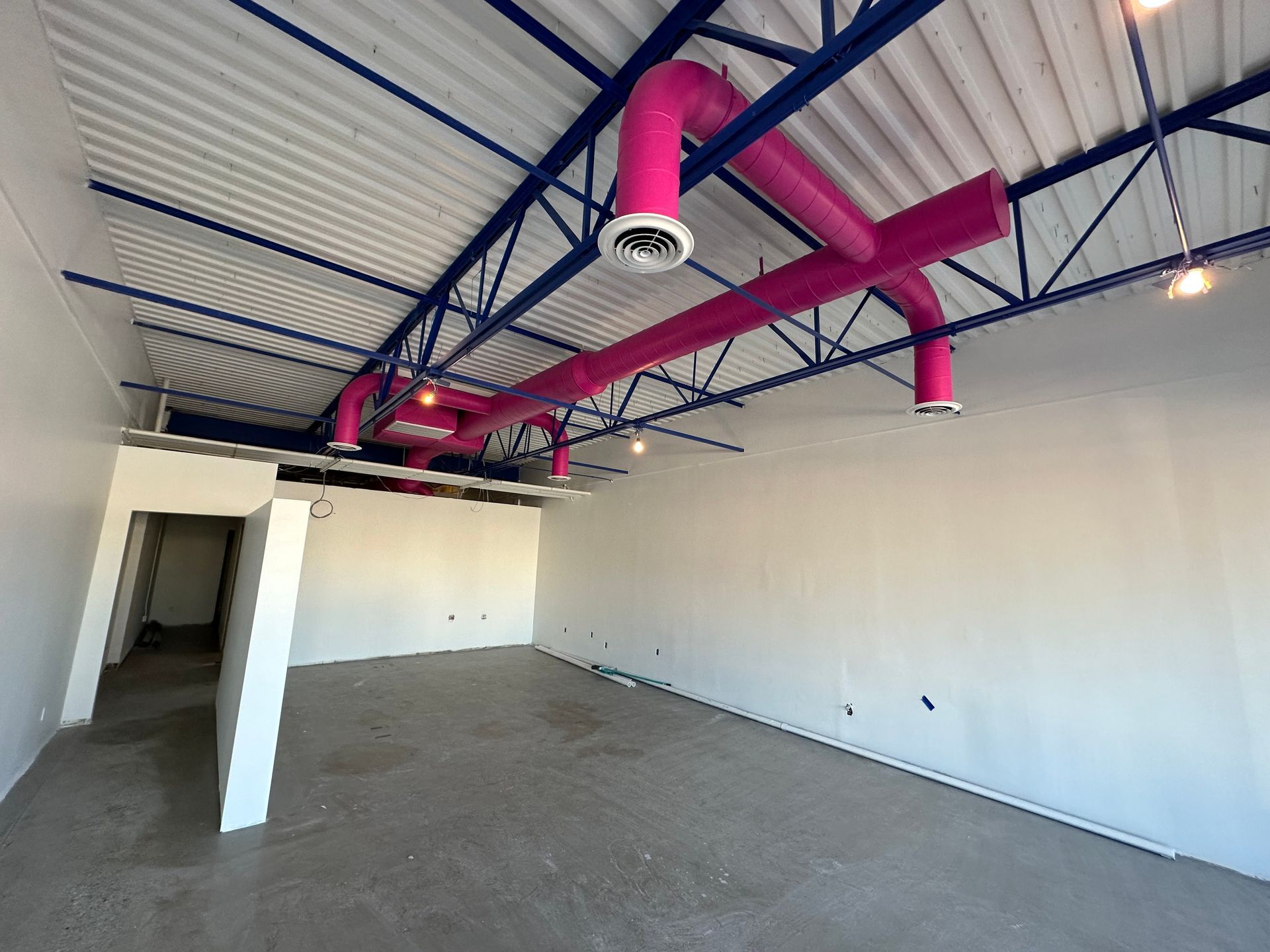 An empty room with pink pipes hanging from the ceiling.