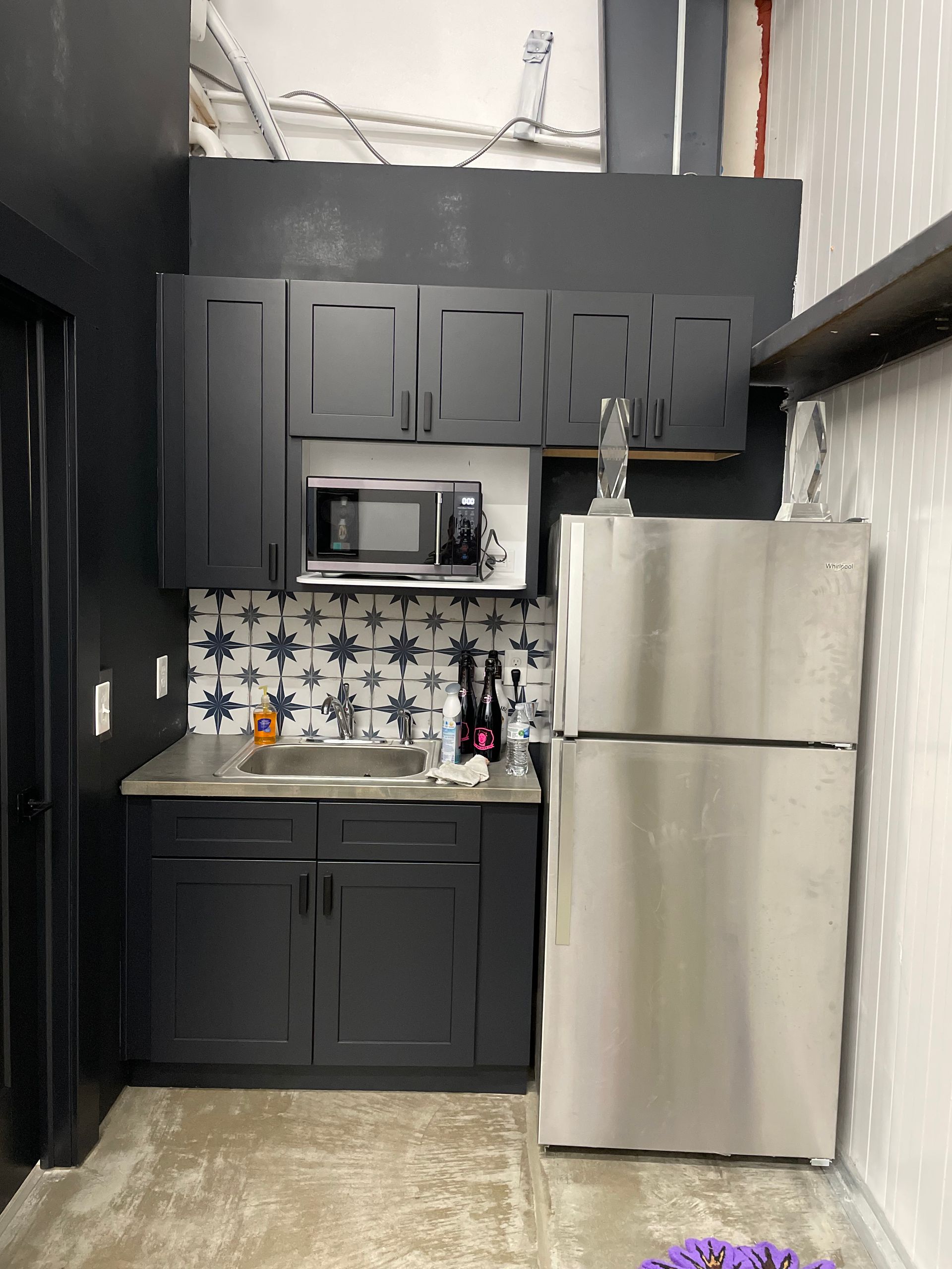 A small kitchen with black cabinets and a stainless steel refrigerator