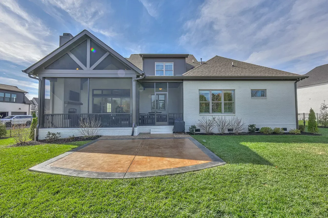 The back of a house with a screened in porch and a driveway.