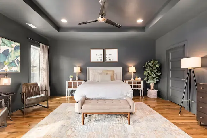 A bedroom with a bed , chairs , lamps and a ceiling fan.