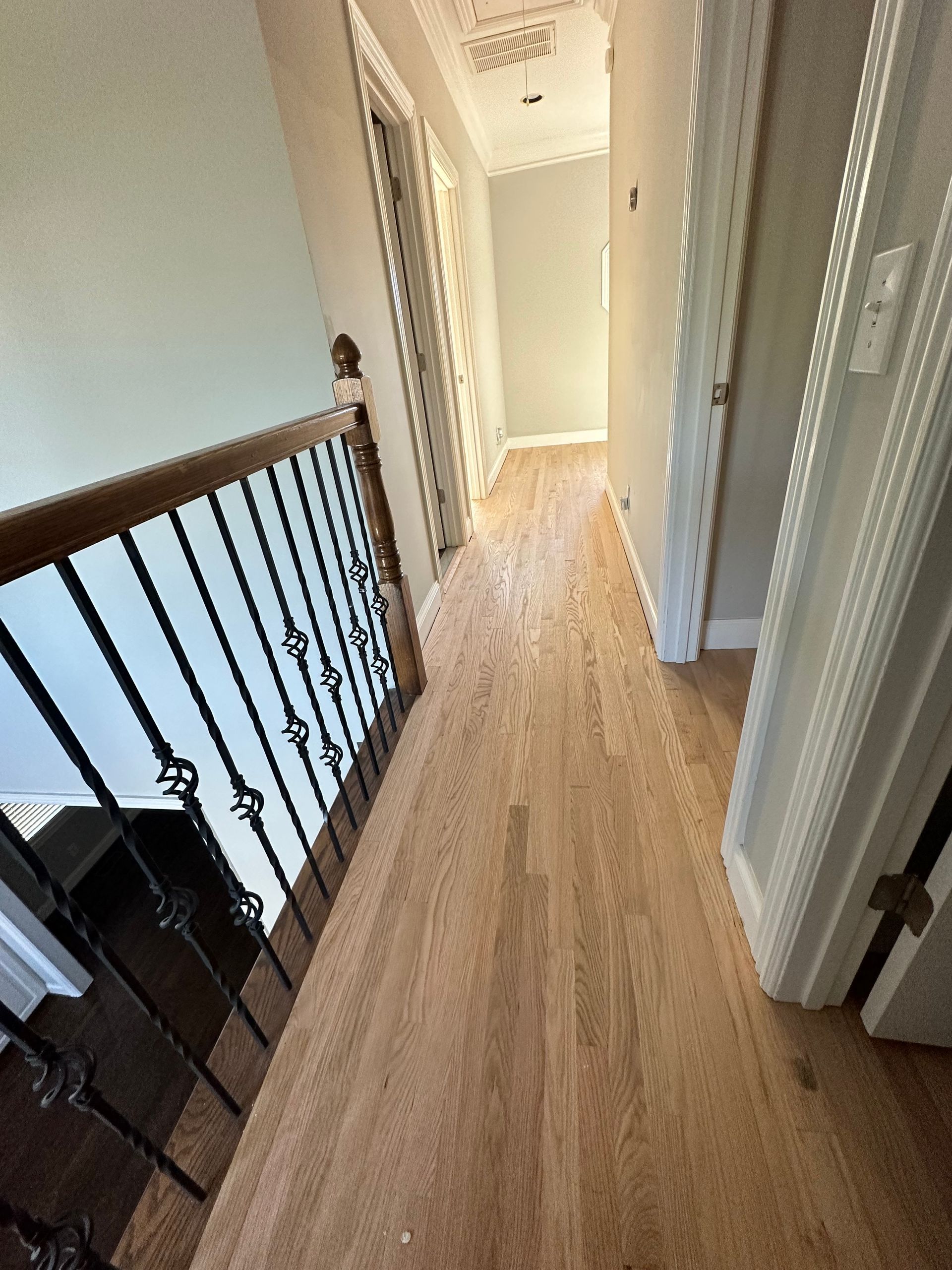 A hallway with hardwood floors and a wrought iron railing.