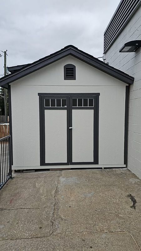 A white shed with black doors is sitting on the side of a building.