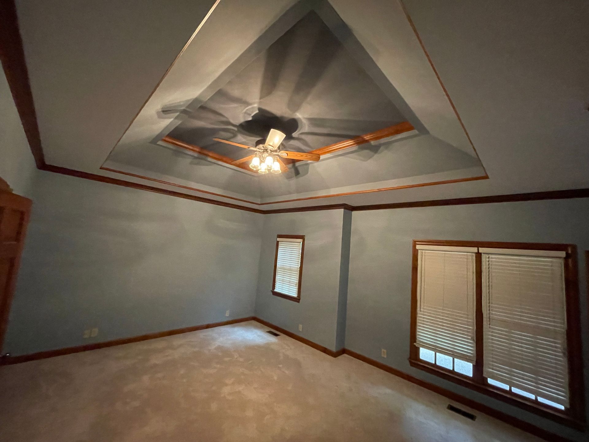 An empty room with a ceiling fan and two windows