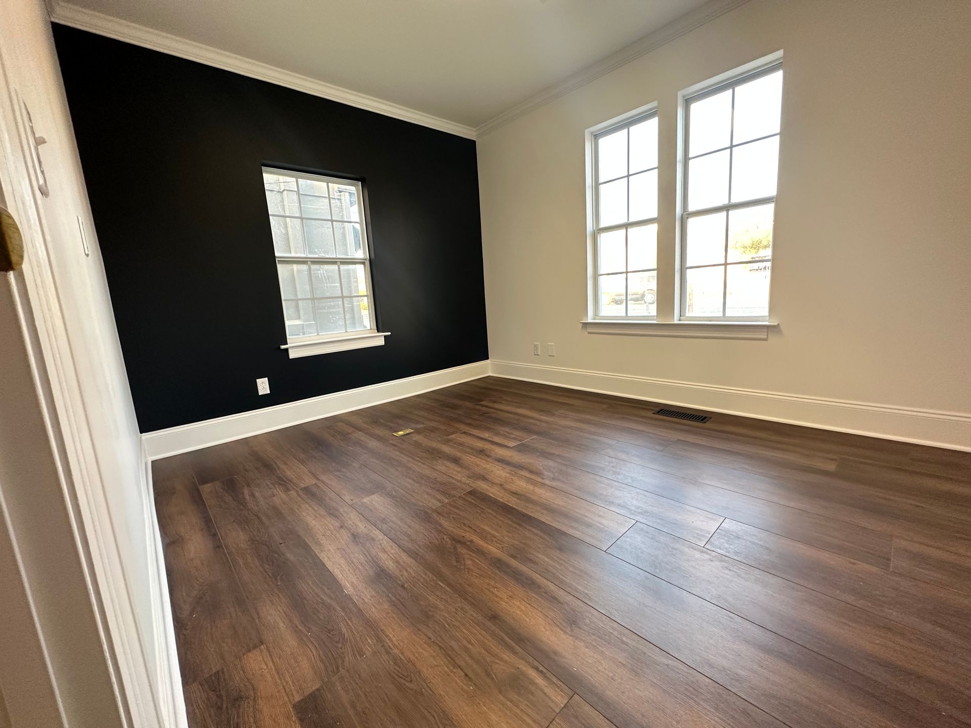An empty room with hardwood floors and two windows.
