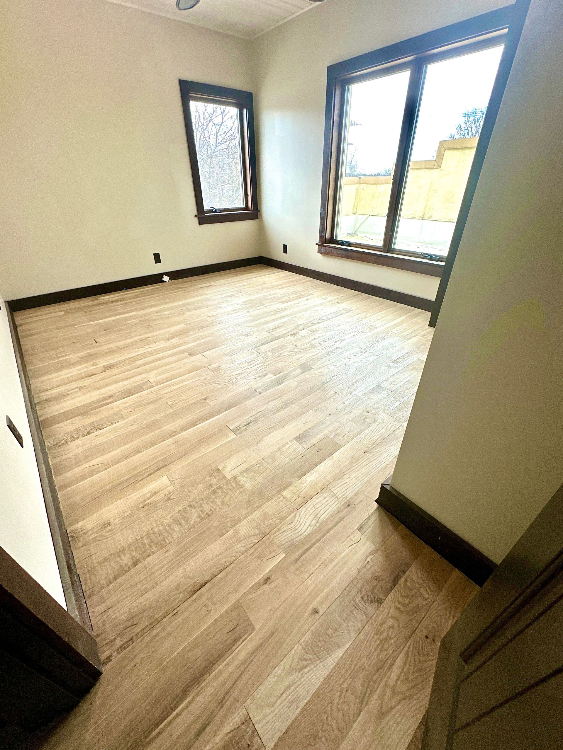 An empty room with hardwood floors and two windows.