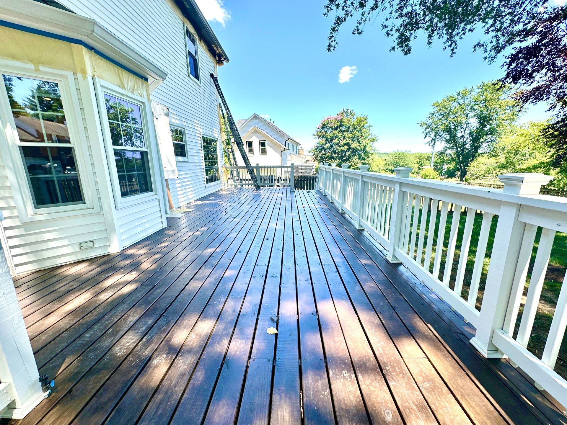 A large wooden deck with a white railing and a white house in the background.