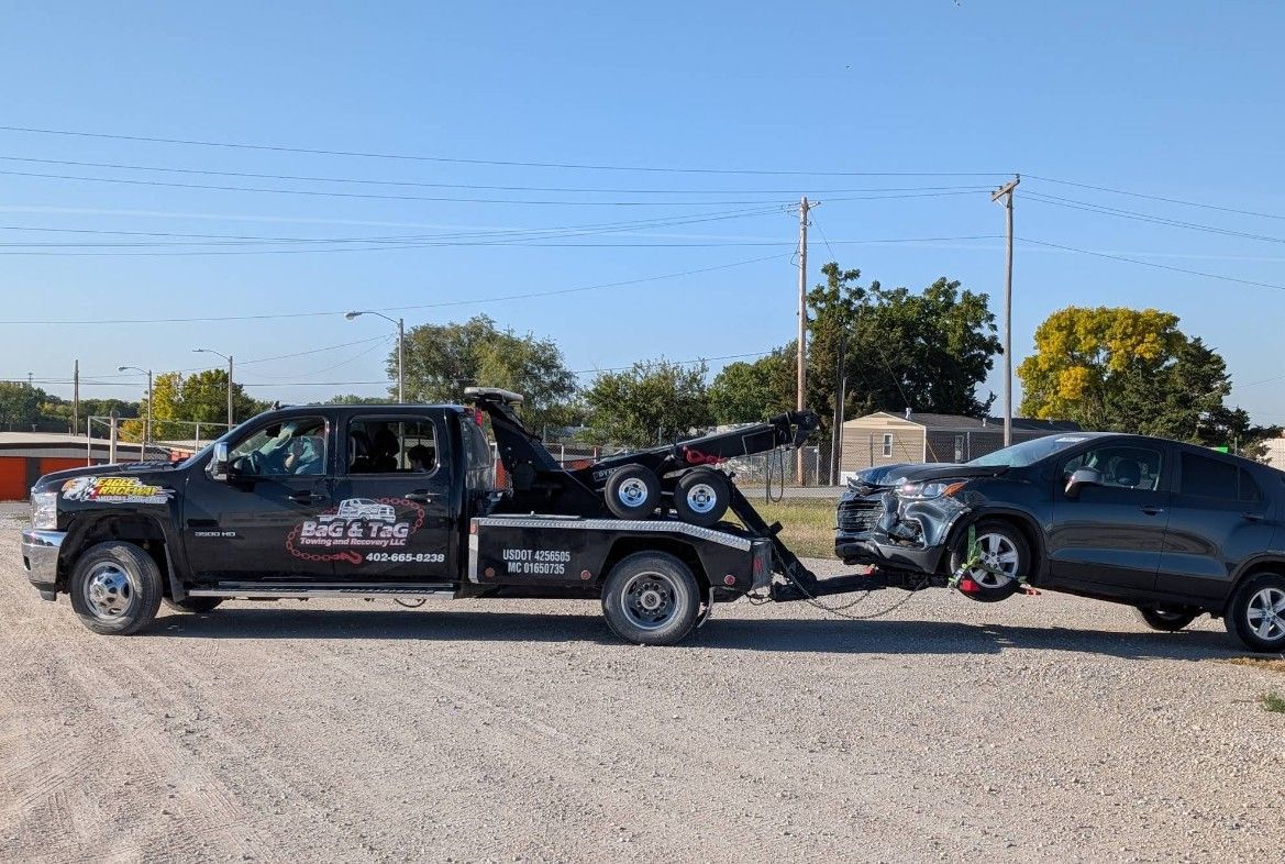Tow truck towing a gray car on a gravel lot under a clear sky.