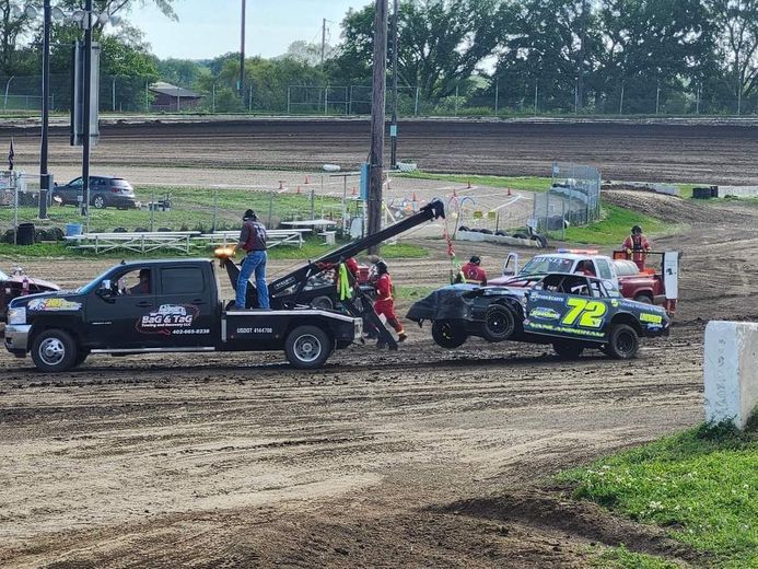 Tow truck lifting race car from dirt track. People assist as car is loaded.