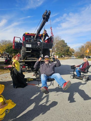 Man swinging from a tow truck, with two others nearby. Clear blue sky, sunny day.