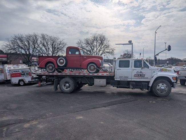 Red vintage pickup truck on a flatbed tow truck on a street.