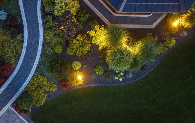 An aerial view of a lush green garden with a house in the background at night.