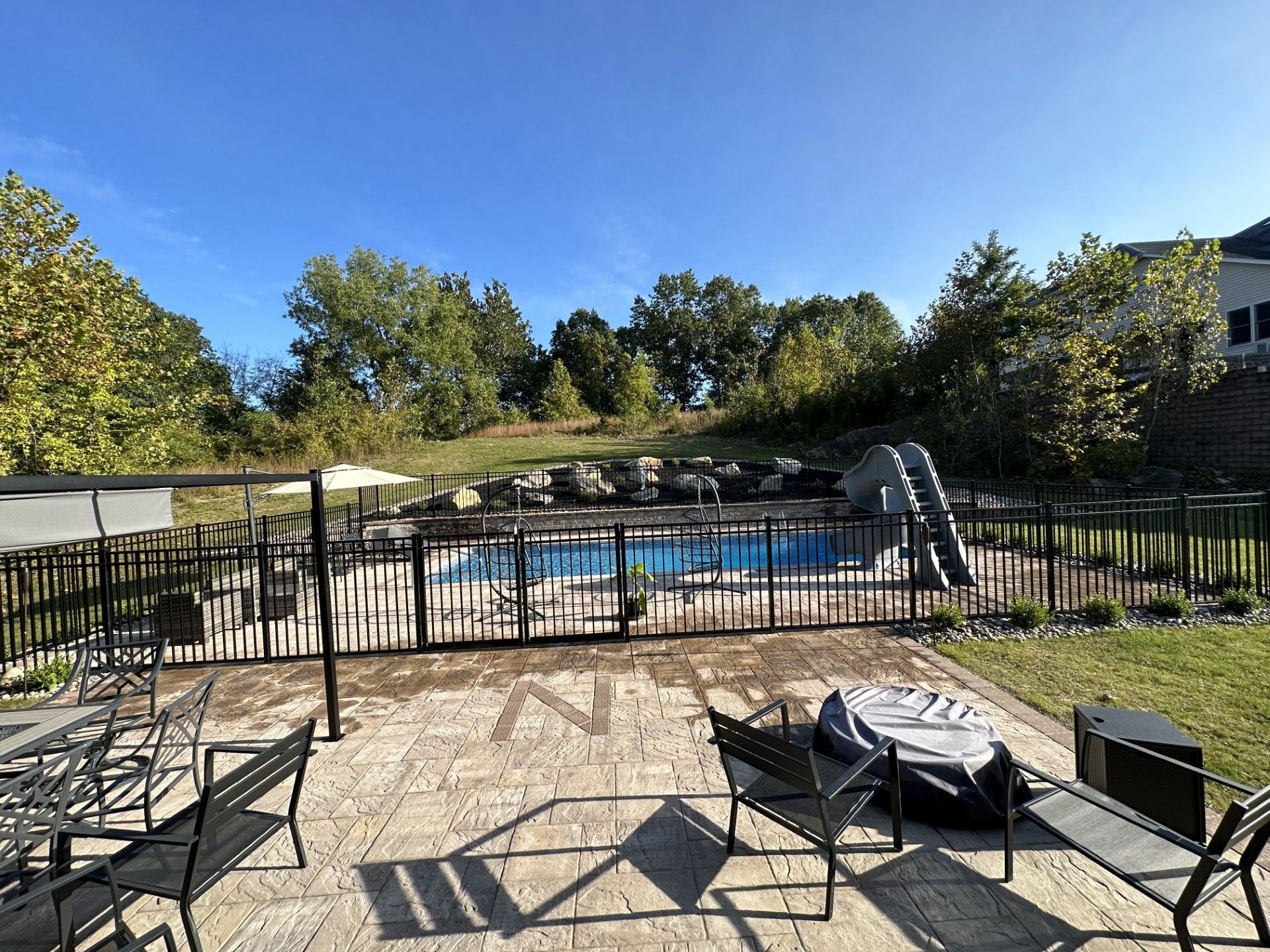 A patio with chairs and umbrellas and a pool in the background.