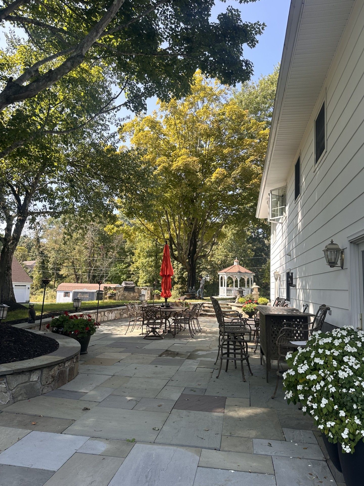 A patio with tables and chairs and an umbrella in front of a house.