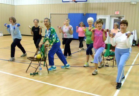 A group of people exercising with dumbbells in a gym.