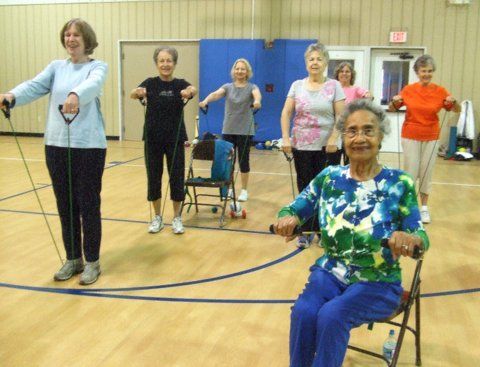 Group of people exercising with resistance bands in a gym. Some seated, some standing.