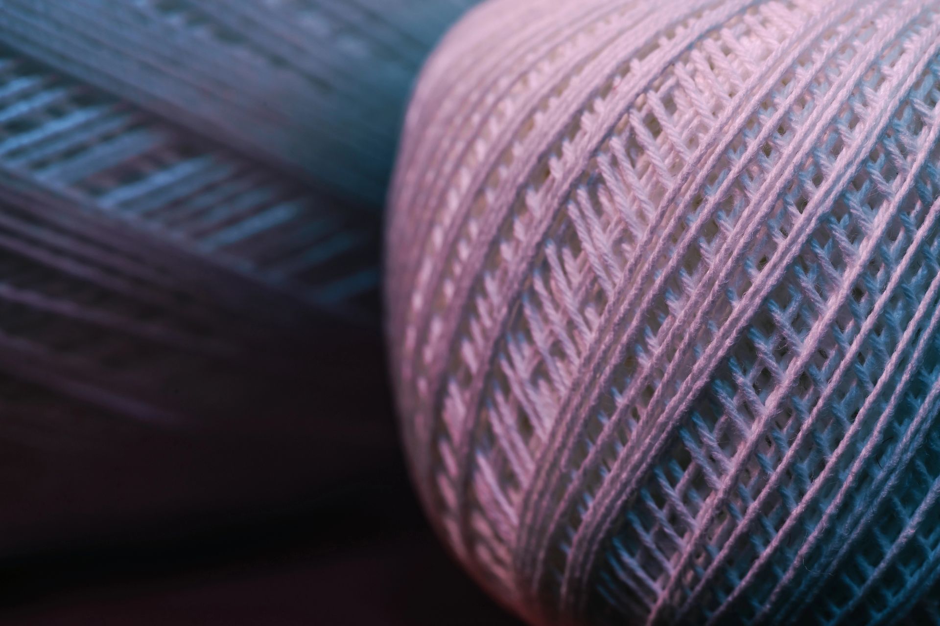 Primo piano di due gomitoli di filo, uno blu e uno rosa, con trama intrecciata visibile.
