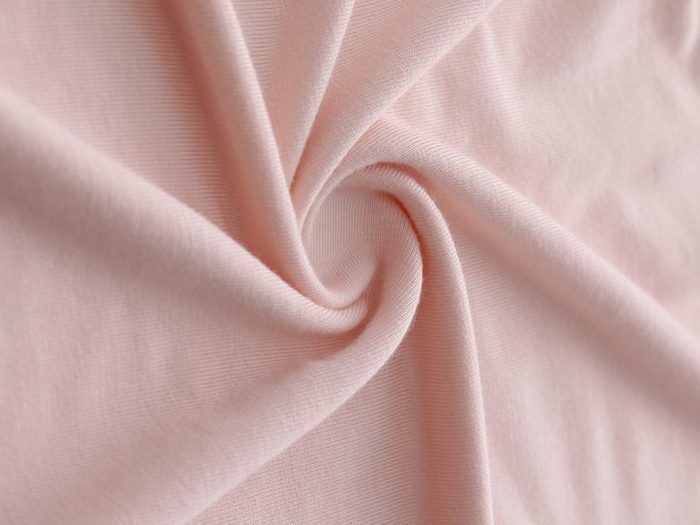 Tessuto rosa pallido, strettamente arrotolato per mostrare la consistenza e le pieghe.