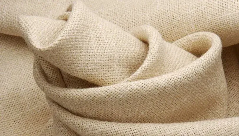 Tessuto di lino testurizzato color crema, drappeggiato e piegato in modo lasco, con fili intrecciati in evidenza.