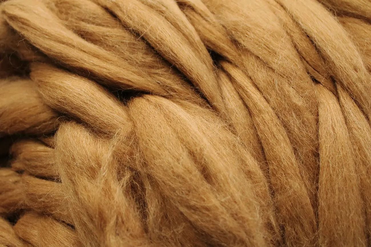 Primo piano di un grosso pezzo di lana cardata color marrone chiaro, strettamente arrotolato.