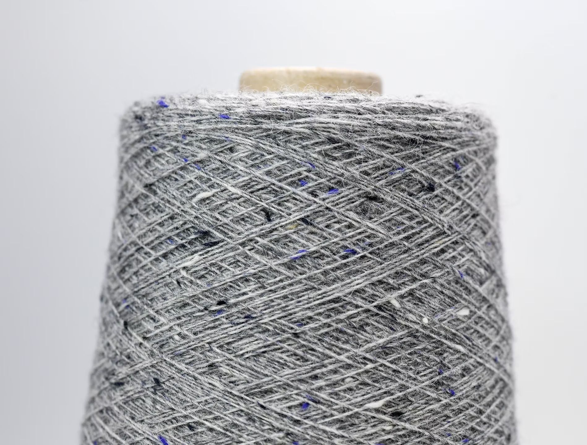 Rocchetto di filato di tweed grigio con macchie blu e bianche.