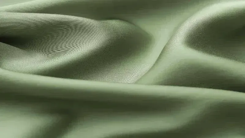 Tessuto di seta verde salvia morbido e fluido, con sottili riflessi e ombre.