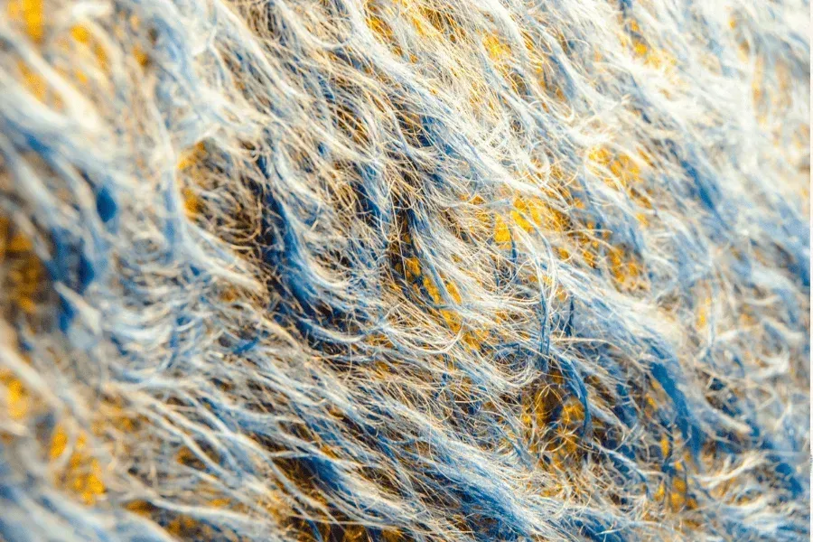 Primo piano di un soffice tessuto; fili blu, bianchi e gialli si intrecciano, creando una superficie strutturata.