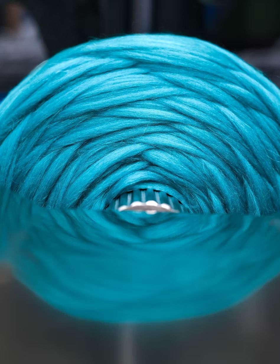Gomitolo di filato turchese, strettamente avvolto, con riflesso nella parte inferiore.