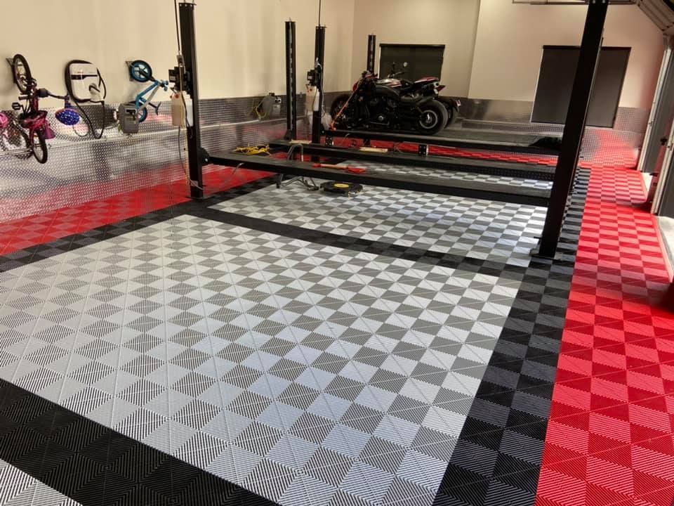 Intérieur de garage avec pont élévateur noir, carrelage à damier et une moto.