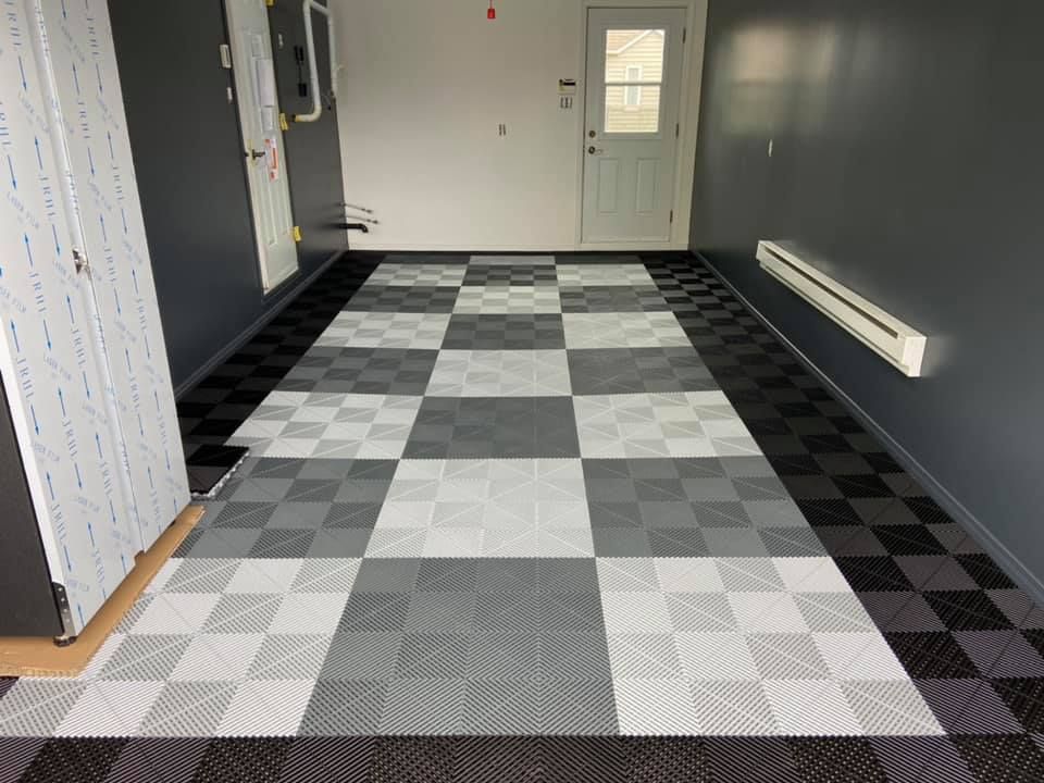 Garage avec sol à damier gris et noir, murs gris foncé, porte blanche et chauffage mural.